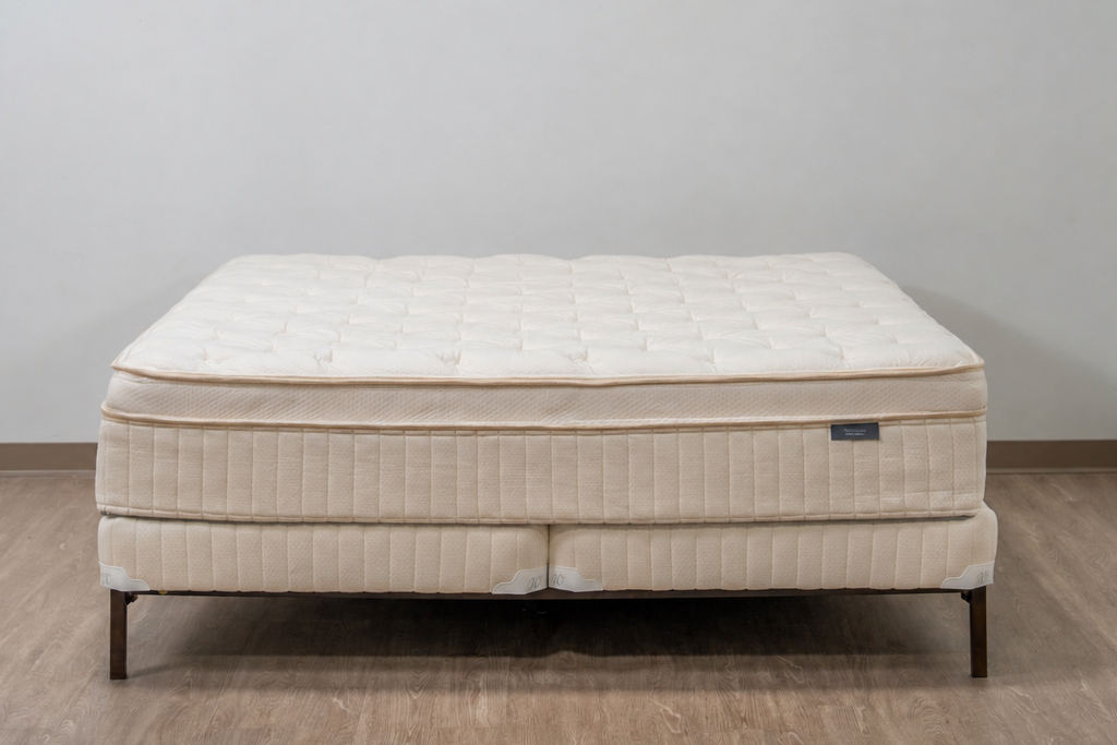 A quilted mattress on a matching upholstered bed frame with dark metal legs, set against a plain light gray wall and wood-look floor.