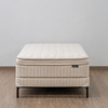 A quilted mattress on a matching upholstered bed frame with dark metal legs, set against a plain light gray wall and wood-look floor.